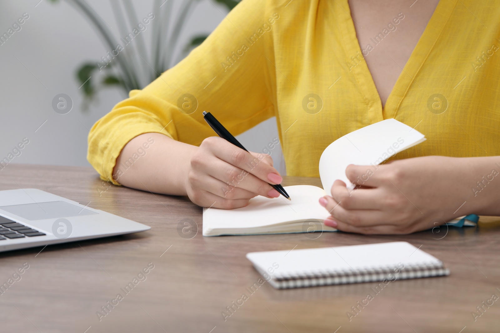 Photo of Woman writing in notebook at wooden table indoors, closeup