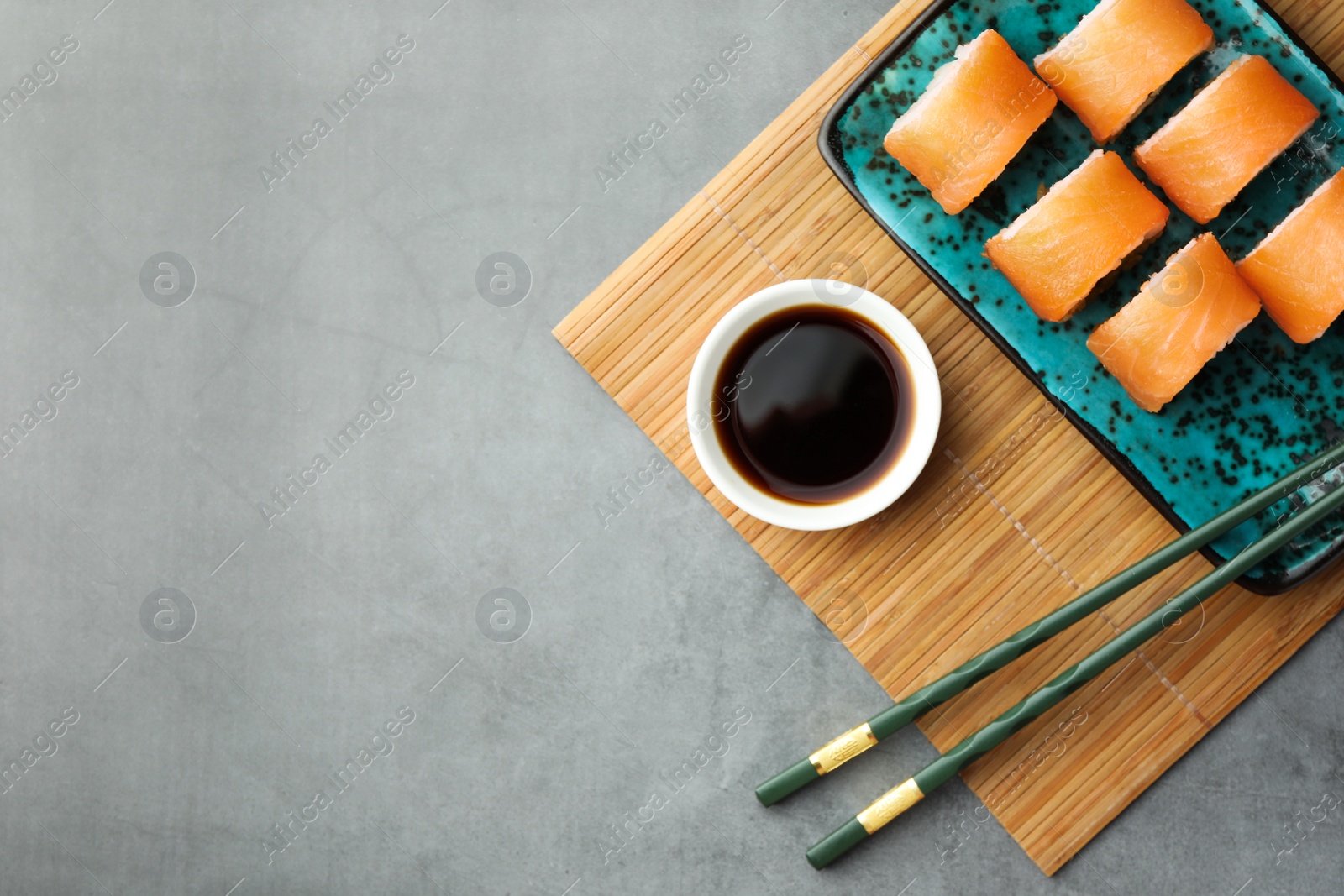 Photo of Tasty soy sauce, chopsticks and sushi rolls with salmon on grey table, top view. Space for text