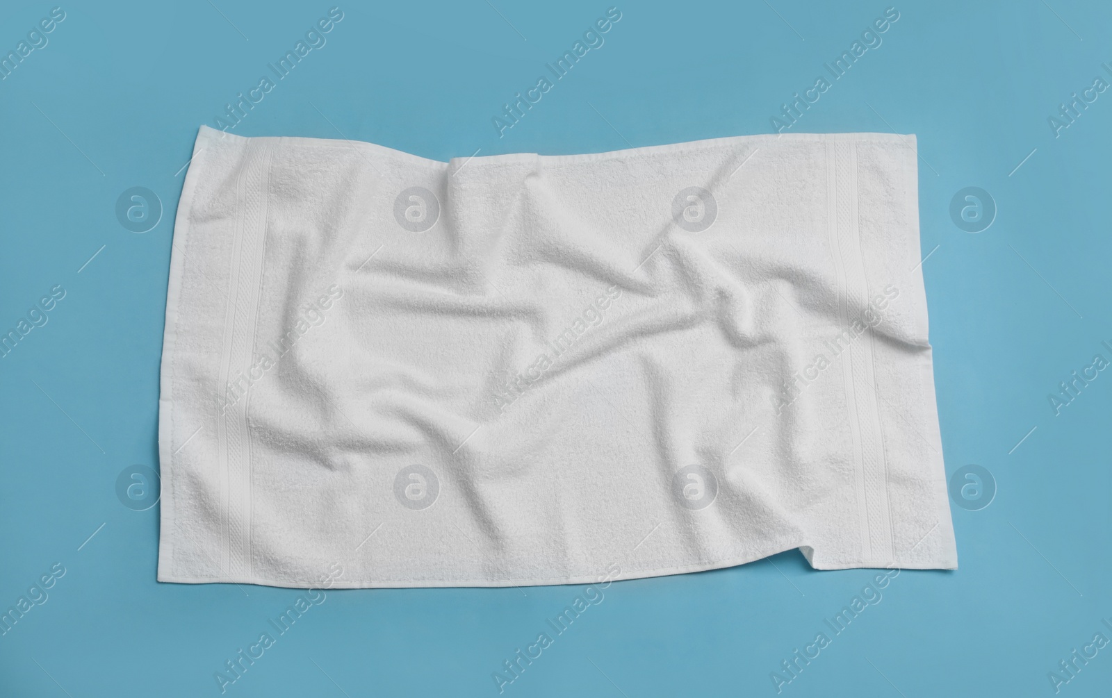 Photo of Crumpled white beach towel on light blue background, top view