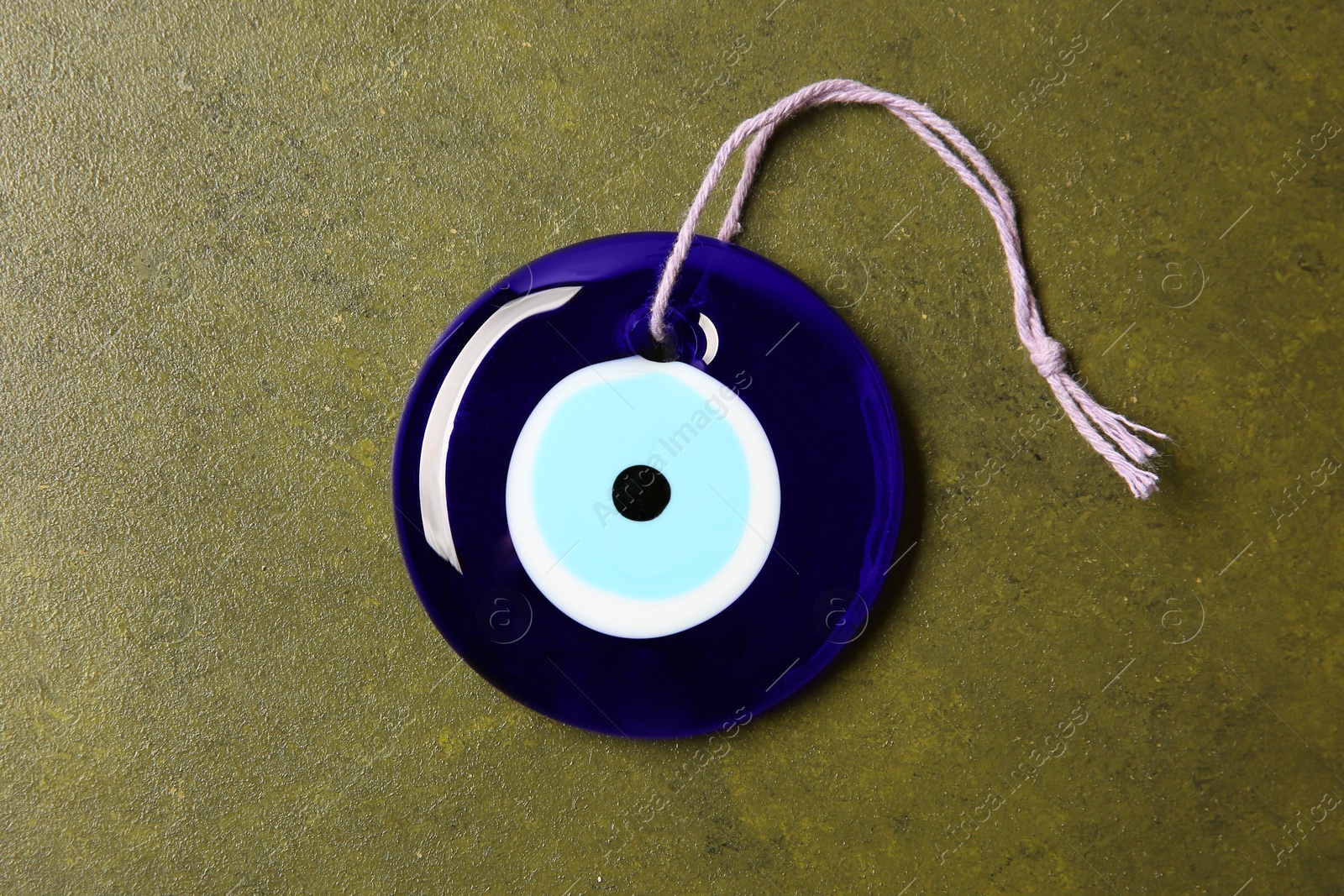 Photo of Evil eye amulet on olive textured table, top view