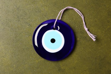 Photo of Evil eye amulet on olive textured table, top view