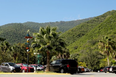 View of mountains, palm trees and parked cars near road