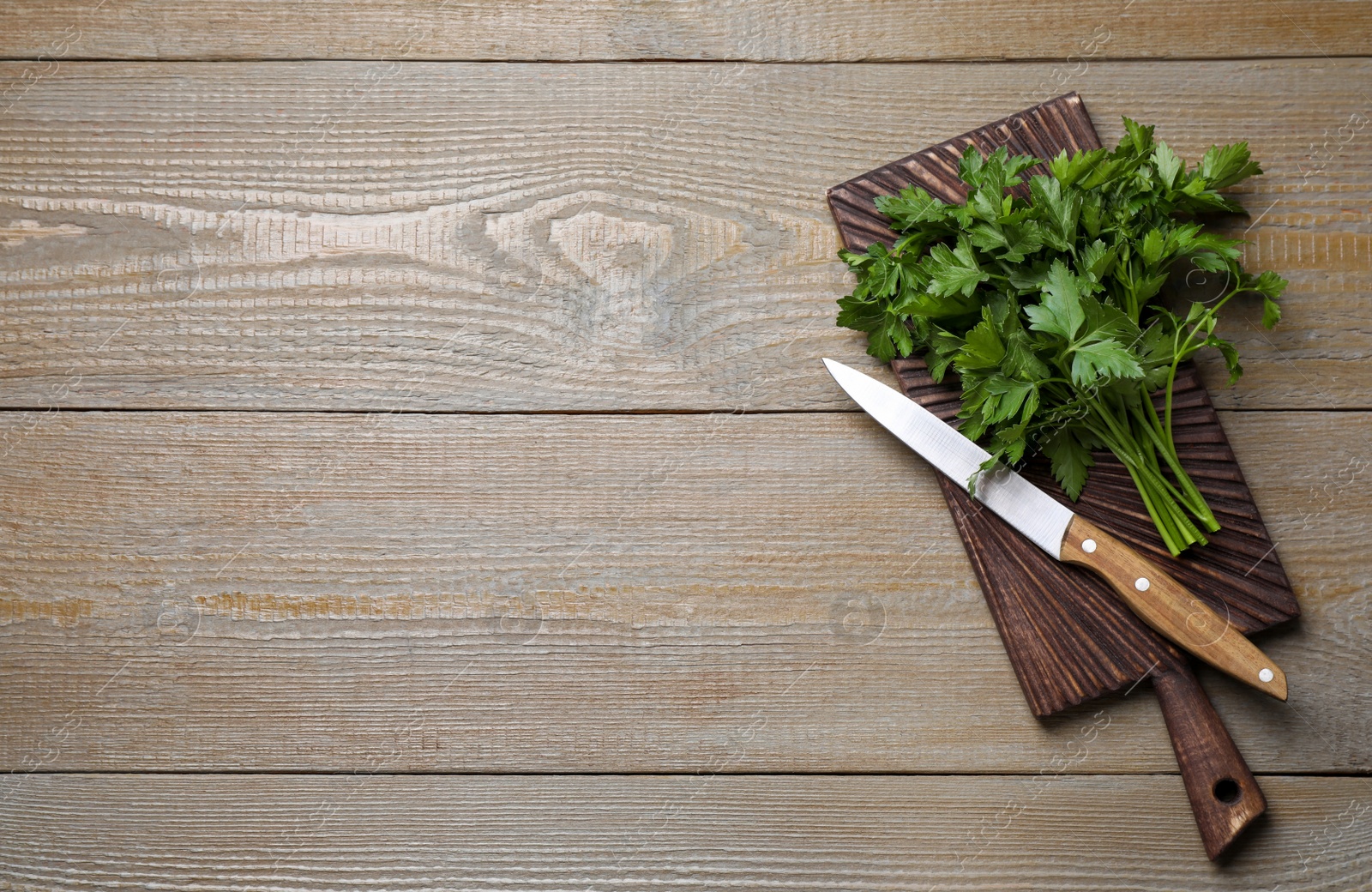 Photo of Board with fresh green parsley and knife on wooden table, top view. Space for text