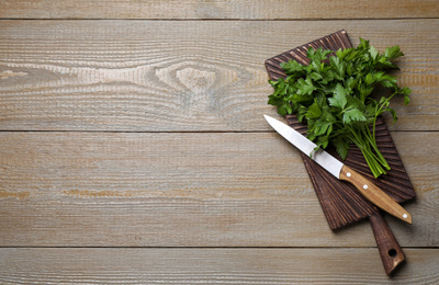 Photo of Board with fresh green parsley and knife on wooden table, top view. Space for text