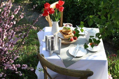 Photo of Beautiful bouquet of tulips and freshly baked waffles on table served for tea drinking in garden