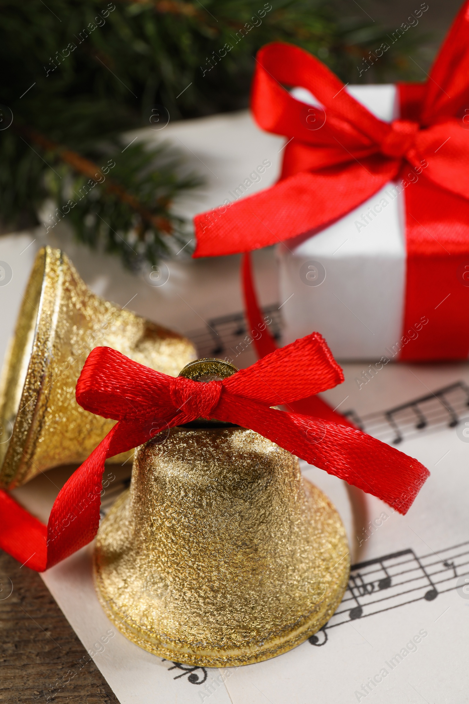 Photo of Bells, gift box and music sheets on wooden table, closeup. Christmas decor
