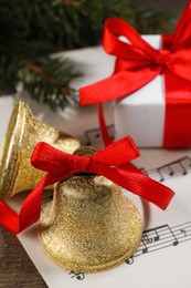 Photo of Bells, gift box and music sheets on wooden table, closeup. Christmas decor
