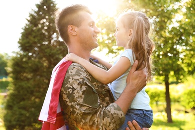 Father in military uniform with American flag holding his little daughter at green park