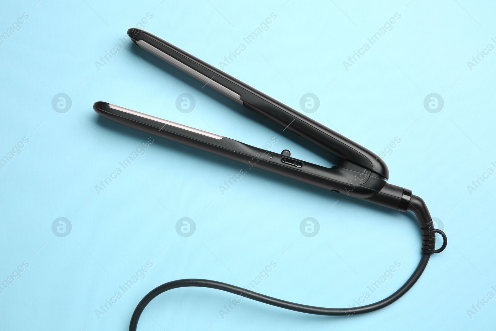 Photo of Modern flat hair iron on light blue background, top view