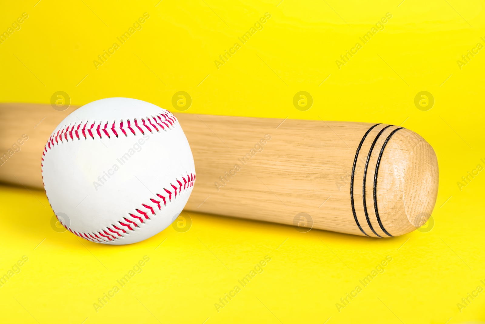 Photo of Wooden baseball bat and ball on yellow background, closeup. Sports equipment