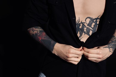 Photo of Young man with tattoos wearing black shirt on dark background, closeup