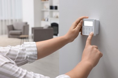 Photo of Man adjusting thermostat on white wall indoors, closeup. Smart home system