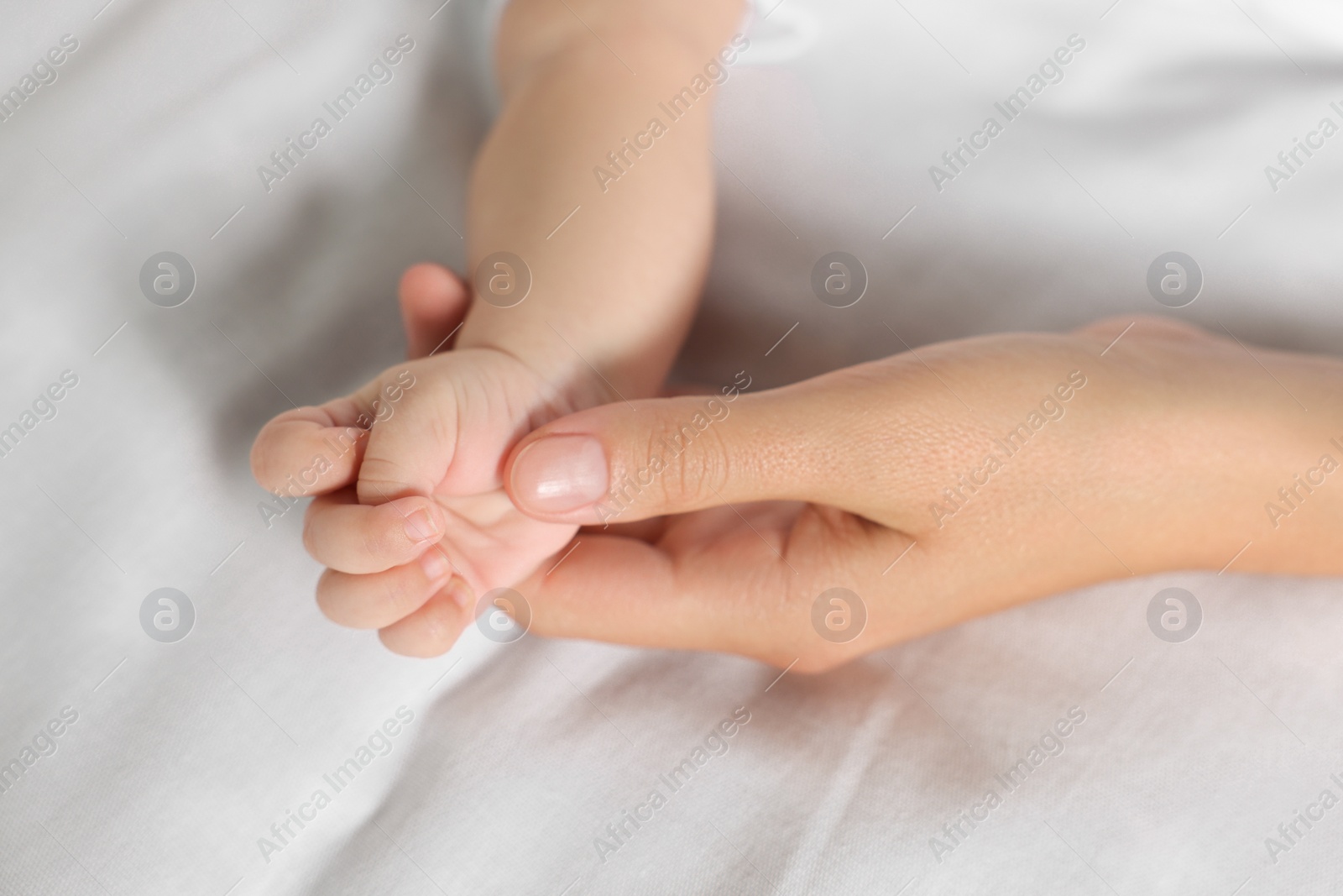 Photo of Mother holding hand of her little baby on bed, closeup