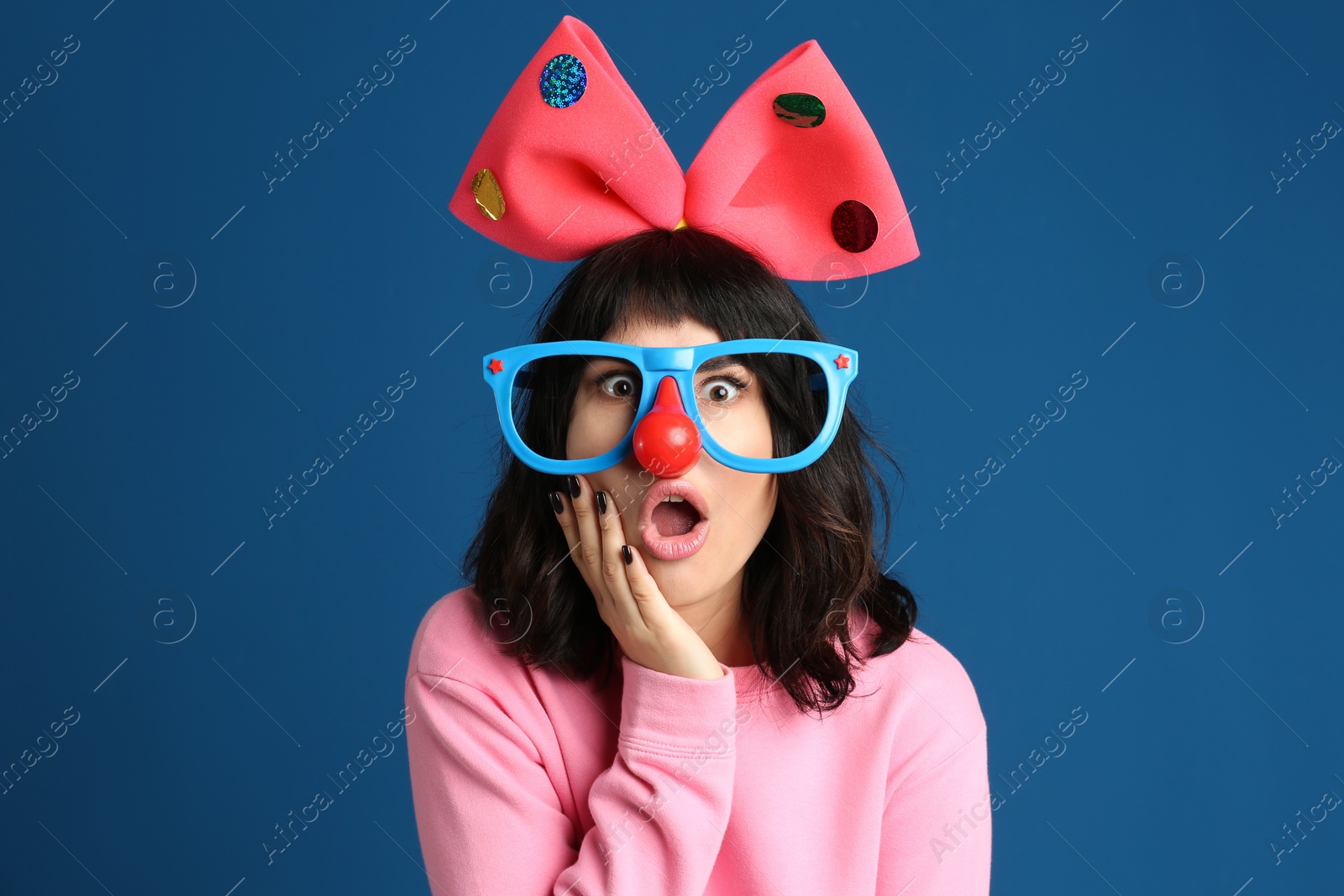 Photo of Emotional woman with funny glasses and large bow on blue background. April fool's day