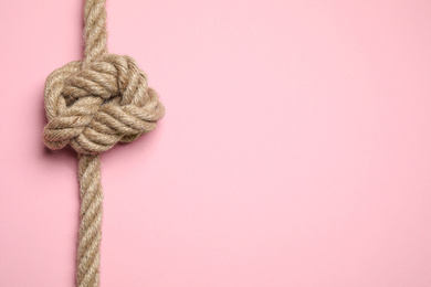 Photo of Top view of linen rope with knot on pink background, space for text. Unity concept