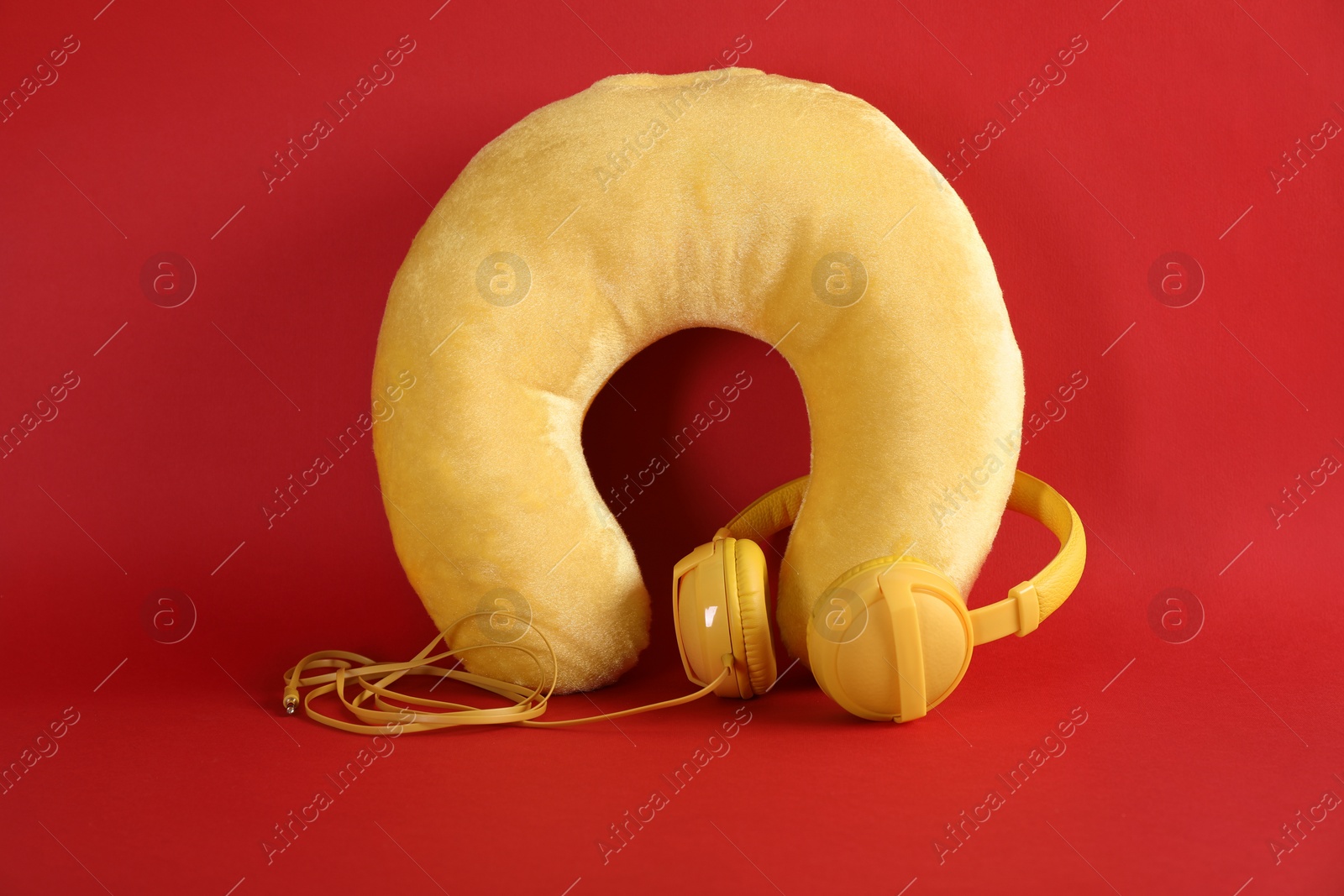 Photo of Yellow travel pillow and headphones on red background