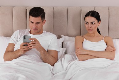 Internet addiction. Man with smartphone ignoring his girlfriend in bedroom