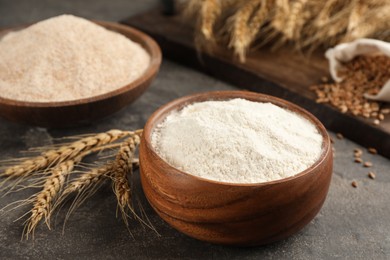 Photo of Wooden bowl of flour and wheat ears on grey table