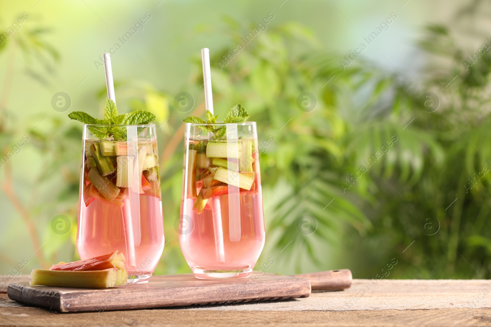 Photo of Glasses of tasty rhubarb cocktail on wooden table outdoors, space for text
