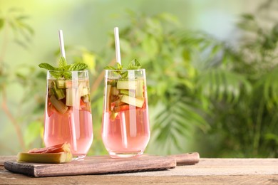 Glasses of tasty rhubarb cocktail on wooden table outdoors, space for text