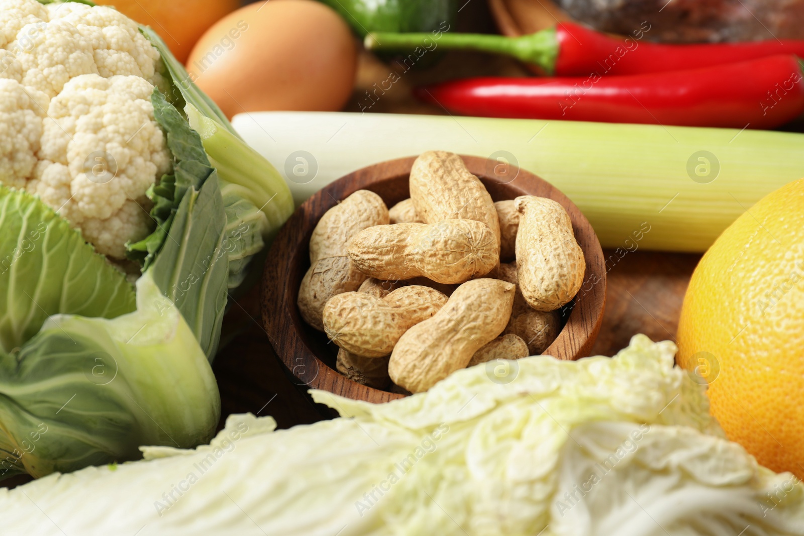 Photo of Healthy meal. Different vegetables and peanuts on wooden table, closeup