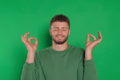 Photo of Young man meditating on green background. Zen concept