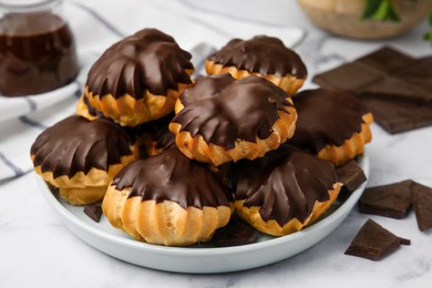 Photo of Delicious profiteroles with chocolate spread on white table, closeup