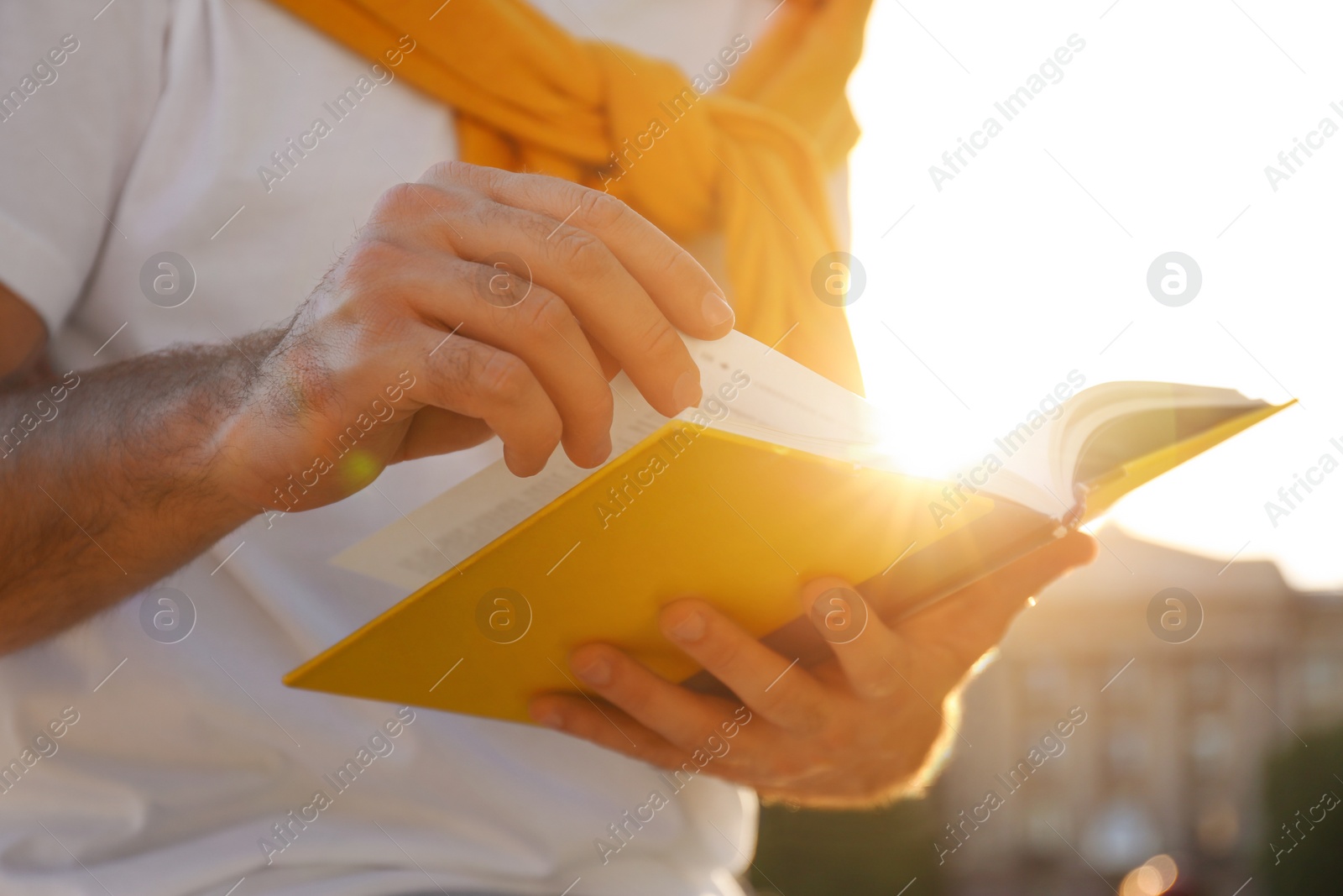 Photo of Young man reading book outdoors on sunny day, closeup