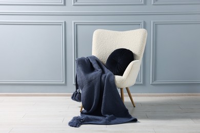 Photo of Comfortable armchair with blanket and pillow near grey wall indoors