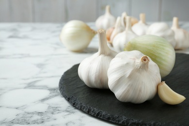 Photo of Slate plate with garlic and onion on marble table. Space for text