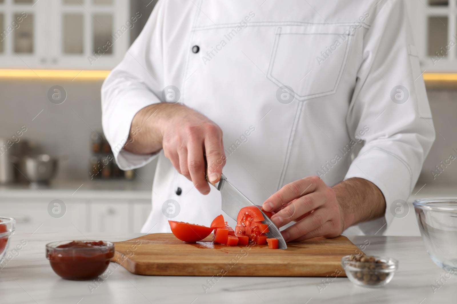 Photo of Professional chef cutting tomatoes at white marble table indoors, closeup