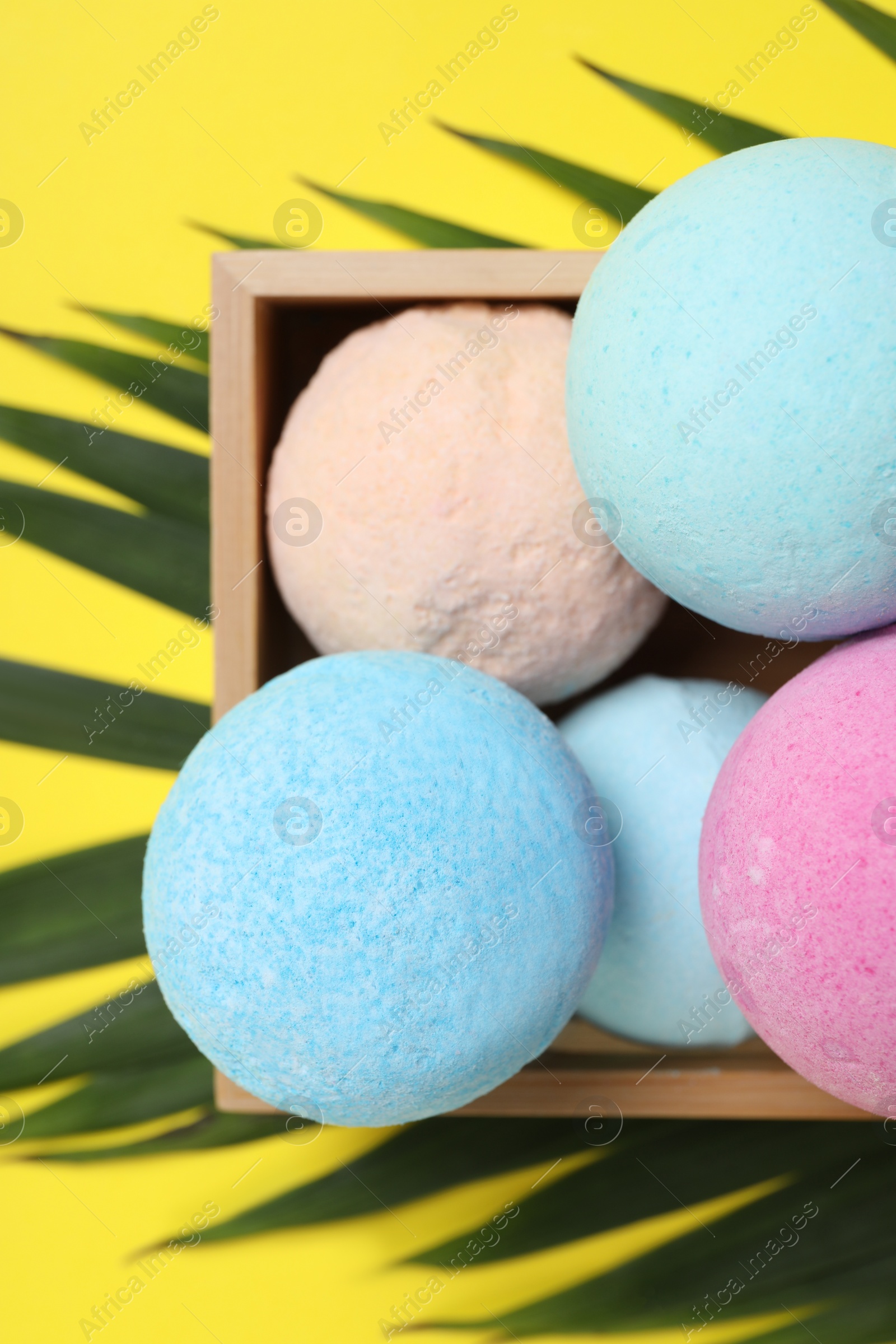 Photo of Wooden crate with bath bombs and green leaf on yellow background, flat lay