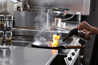 Photo of Female chef cooking meat with manual gas burner on stove in restaurant kitchen, closeup