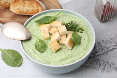 Delicious spinach cream soup with croutons in bowl on white tiled table