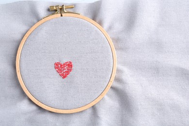 Photo of Embroidered red heart on gray cloth with hoop, top view. Space for text