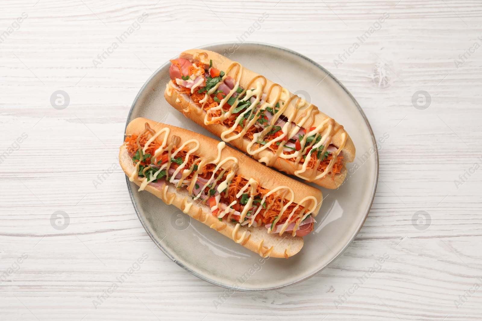 Photo of Delicious hot dogs with bacon, carrot and parsley on white wooden table, top view