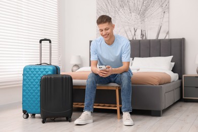Smiling guest with smartphone and suitcase in stylish hotel room