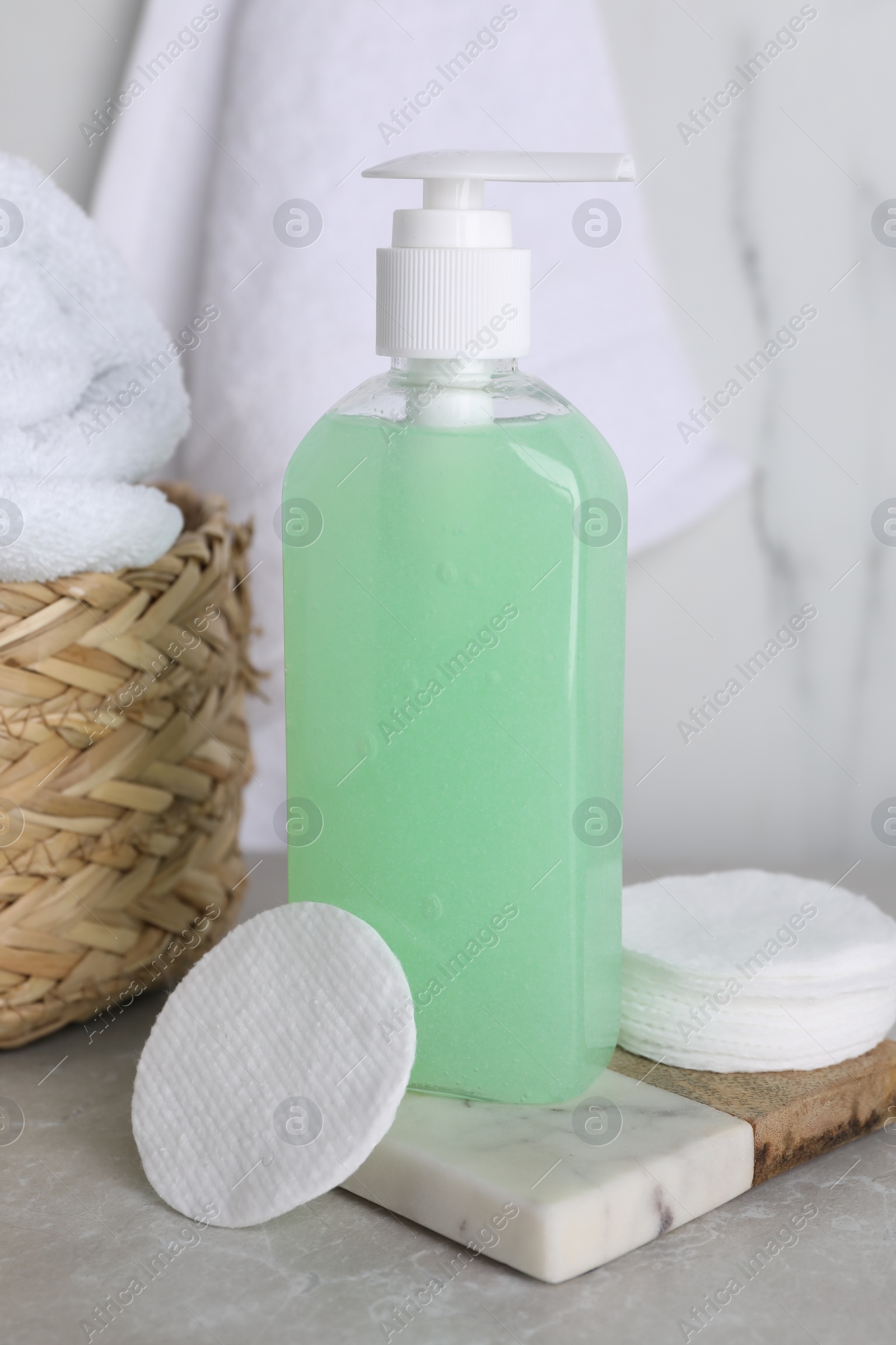 Photo of Bottle of face cleansing product and cotton pads on light grey table