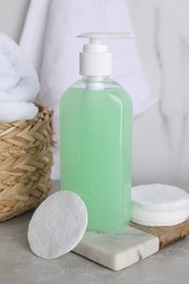 Photo of Bottle of face cleansing product and cotton pads on light grey table
