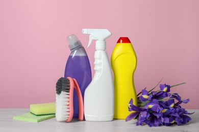 Different cleaning supplies and beautiful spring flowers on white wooden table against light pink background