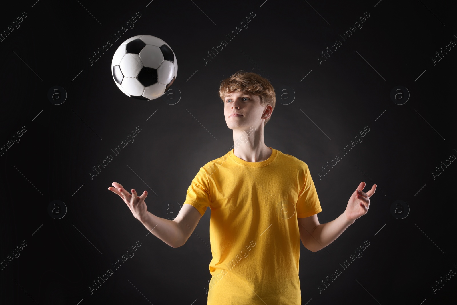 Photo of Teenage boy playing with soccer ball on black background