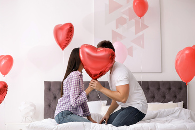 Photo of Romantic couple hiding behind heart shaped balloon in bedroom. Valentine's day celebration