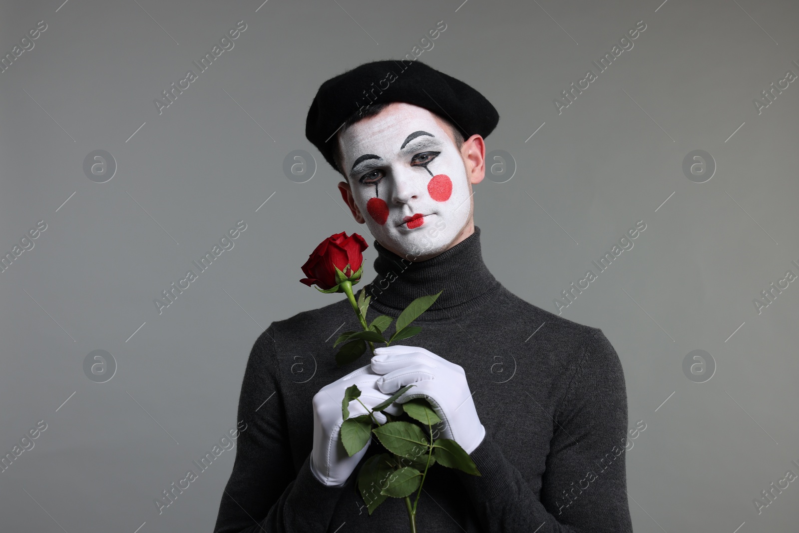 Photo of Portrait of mime artist with red rose on grey background