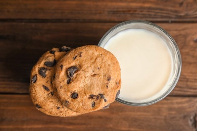Photo of Chocolate chip cookies and glass of milk on wooden background, top view