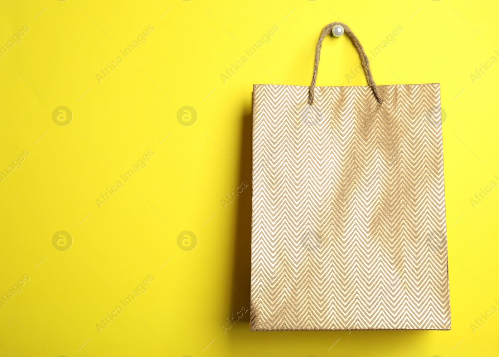 Photo of Gold shopping paper bag on yellow background, space for text