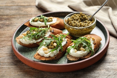 Photo of Plate with tasty bruschettas and pesto sauce on wooden table