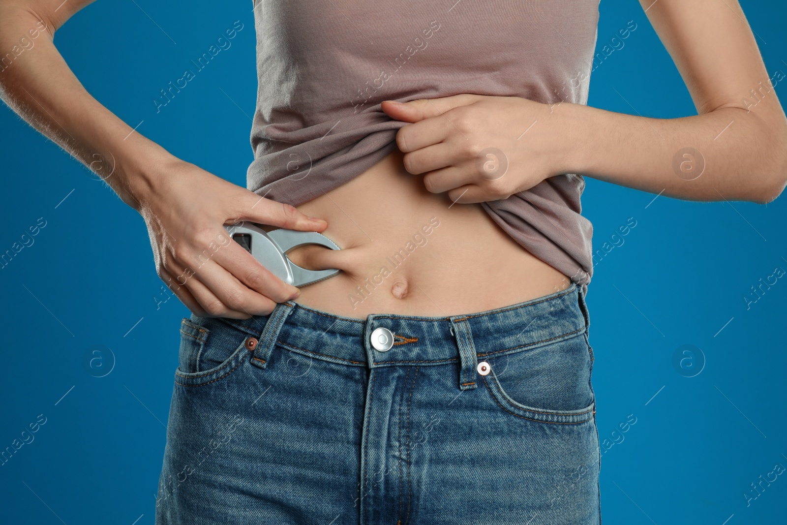 Photo of Young woman measuring body fat with caliper on blue background, closeup