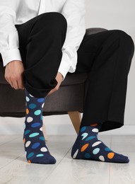 Photo of Man putting on colorful socks indoors, closeup