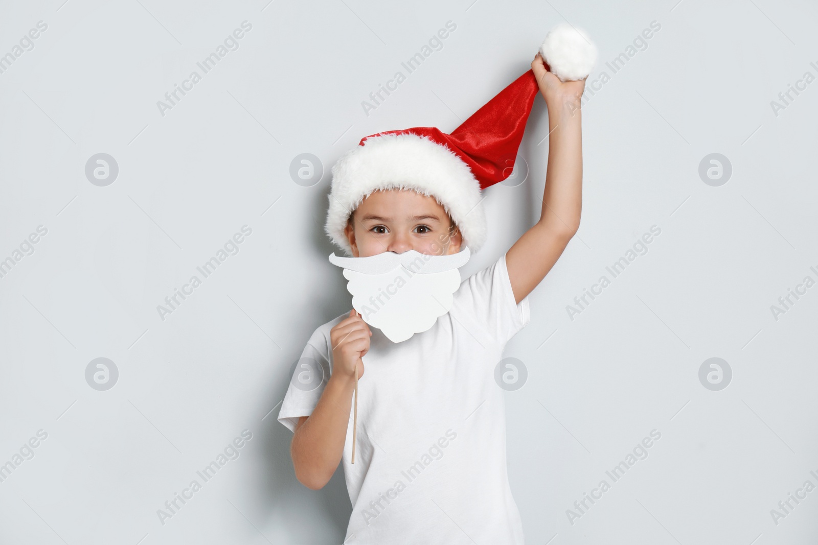 Image of Cute little boy with Santa hat and white beard prop on white background. Christmas celebration