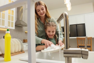 Photo of Mother and daughter washing plate above sink in kitchen, view from outside